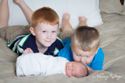 newborn with brothers on bed