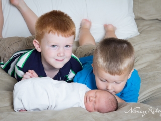 newborn with brothers on bed